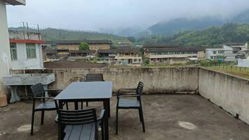 Una terraza en la azotea con una mesa y sillas, con vistas a un pueblo y montañas.