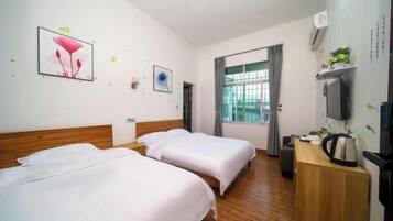 A hotel room with two beds, a wooden headboard, a desk with a kettle, a TV, and a window with curtains.