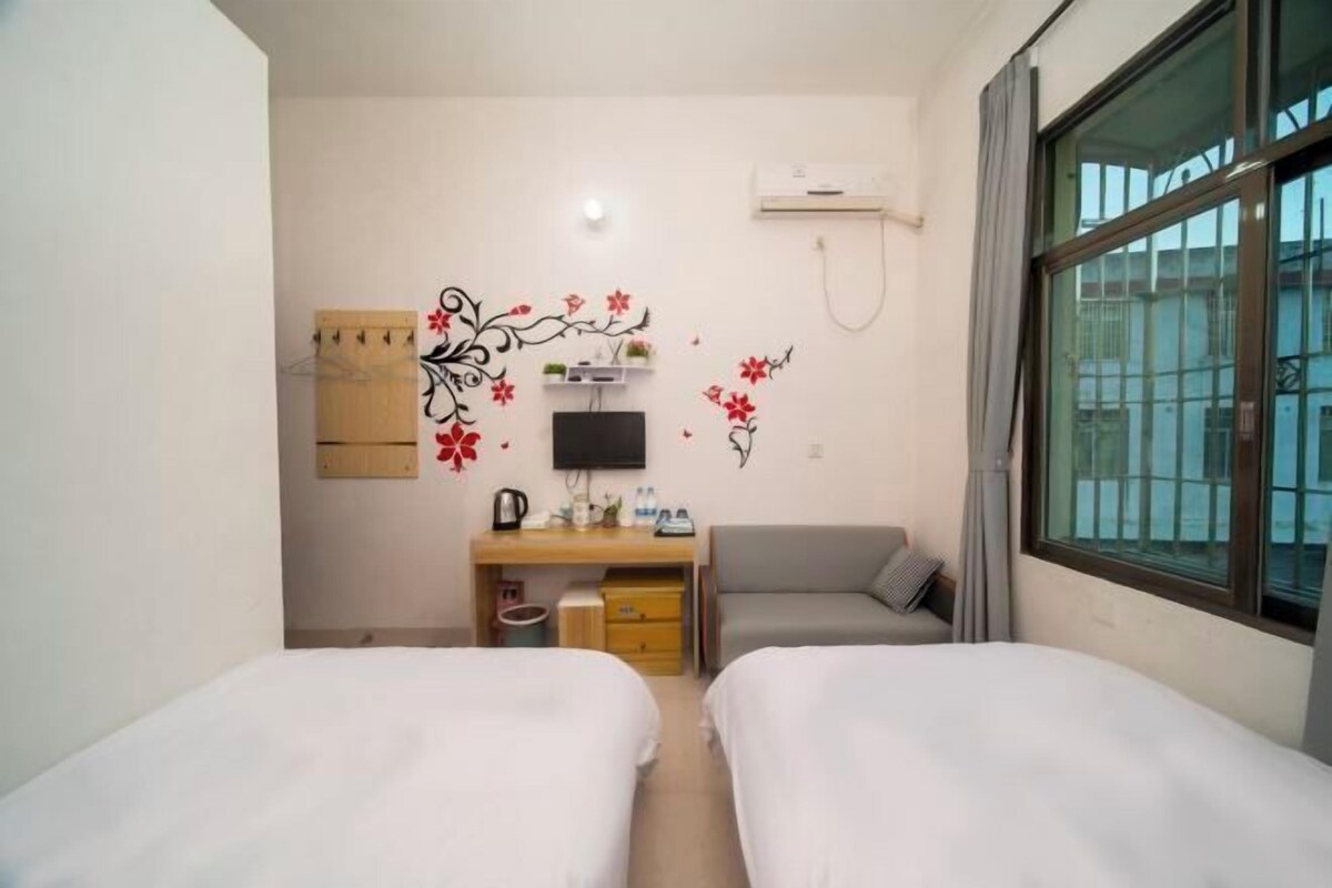 Hotellihuone, jossa on kaksi sänkyä, työpöytä, jossa on televisio, pieni oleskelualue ja ikkuna, josta on näkymä.