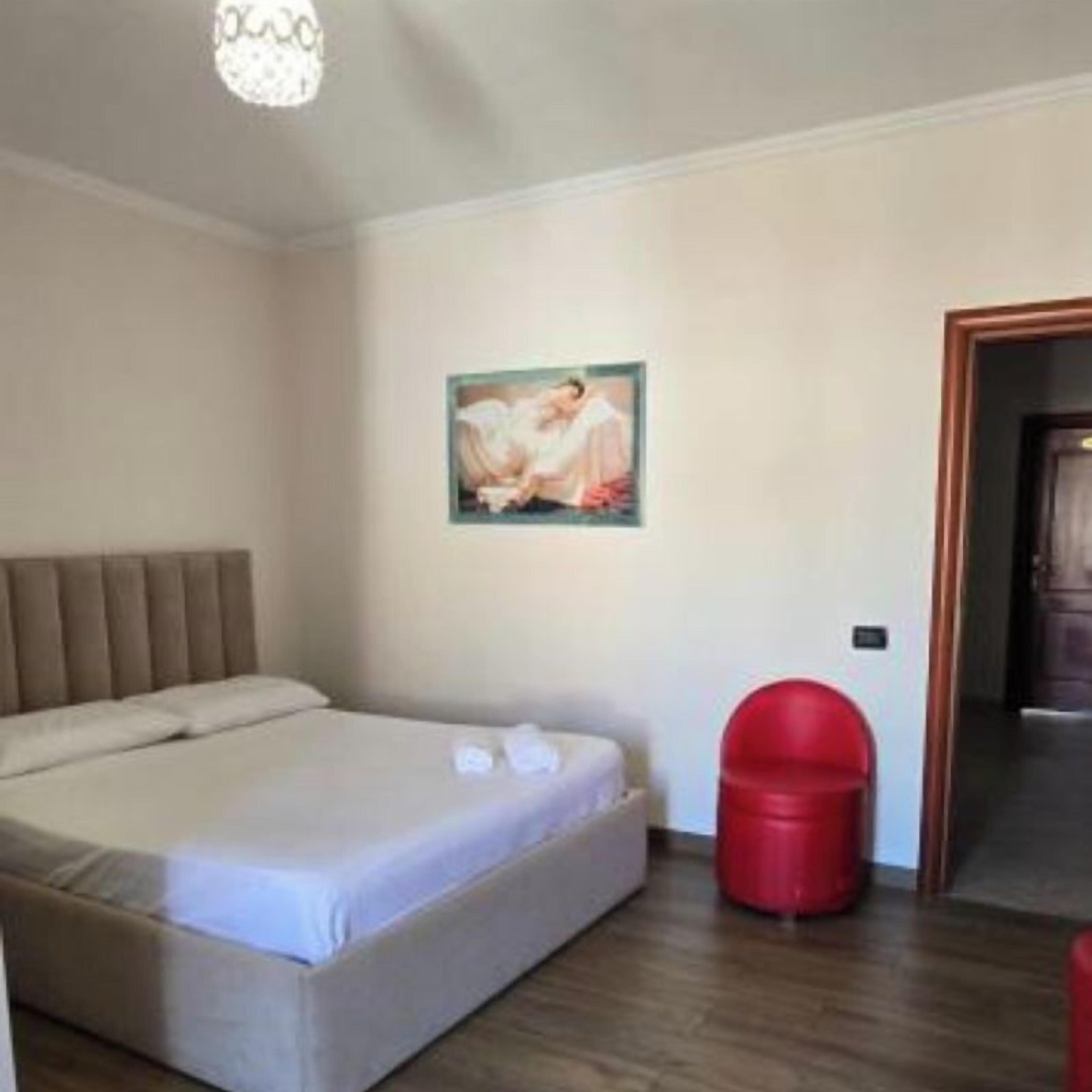 Een slaapkamer met een bed, een schilderij aan de muur en een rode afvalbak.