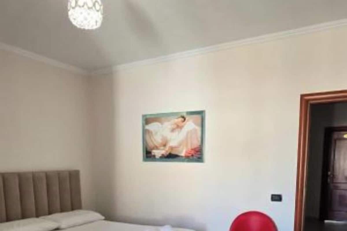 A bedroom with a bed, a painting on the wall, and a red trash bin.