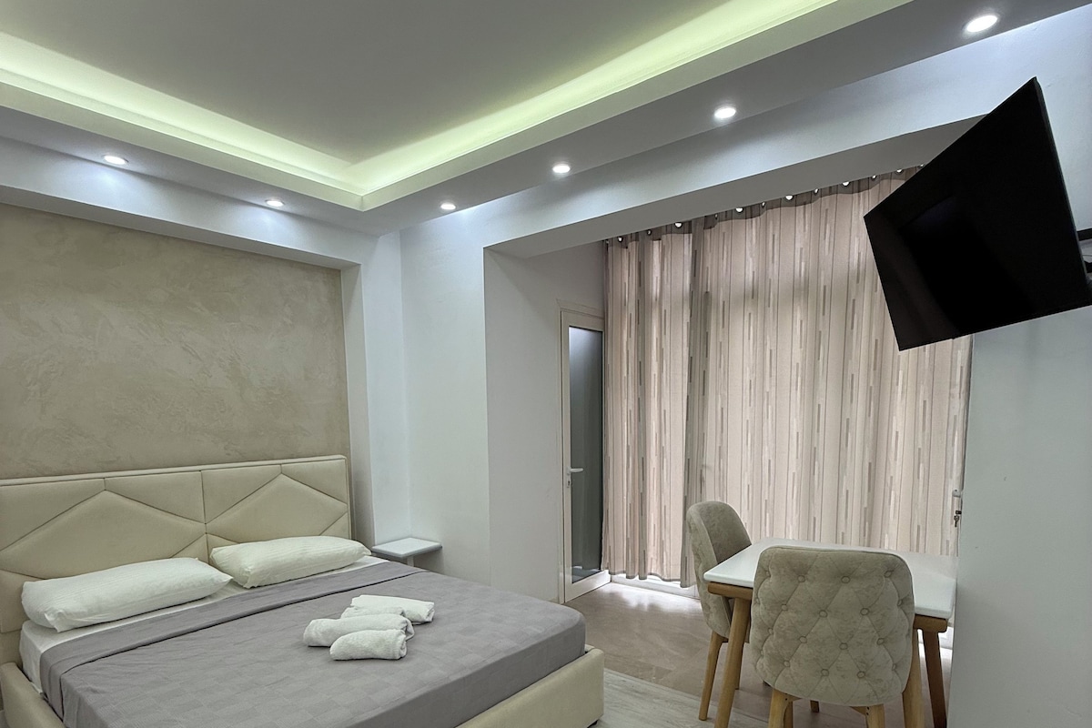 Un dormitorio moderno con cama, mesita de noche, silla y televisor montado en la pared.