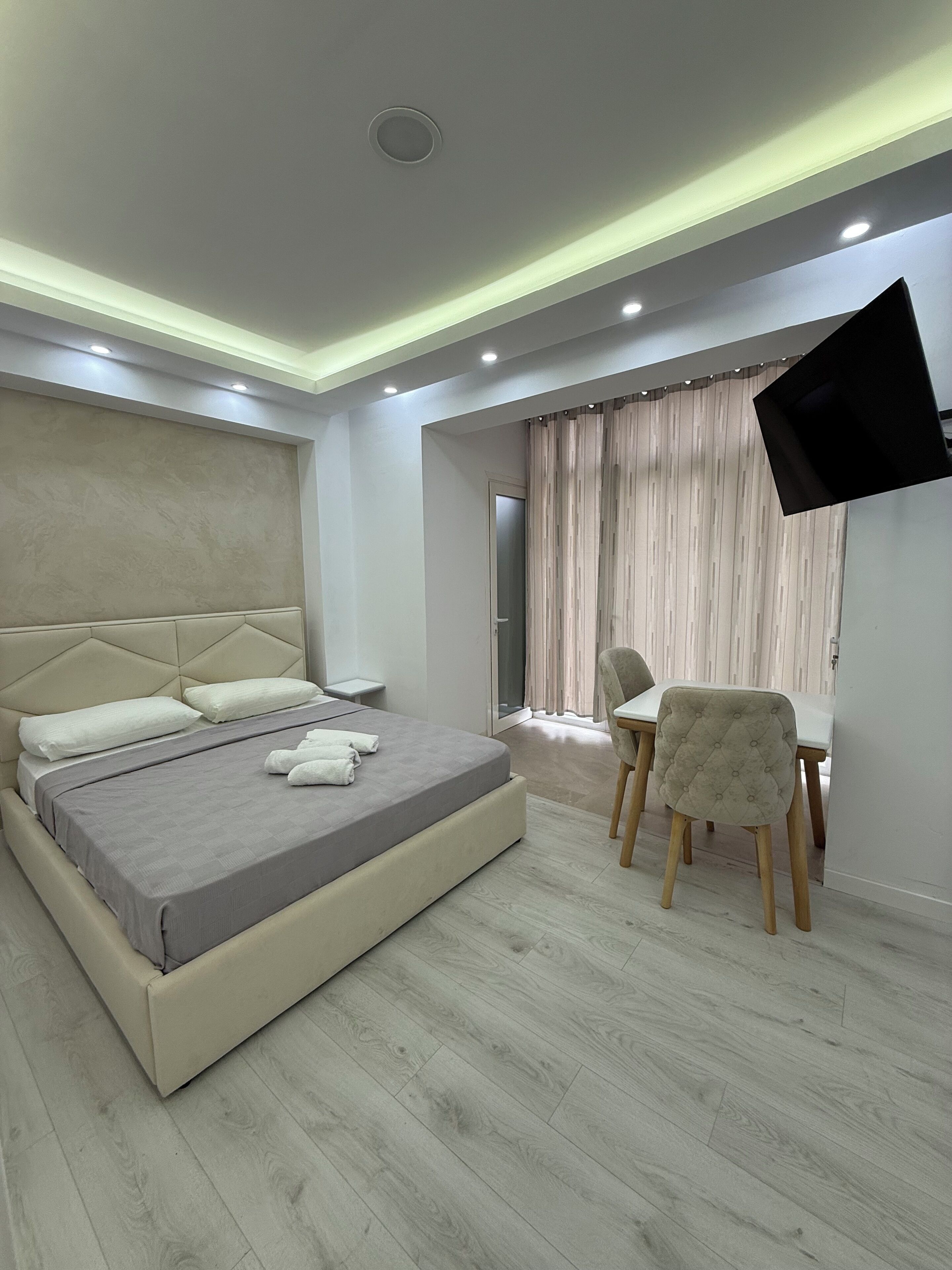 Een moderne slaapkamer met een bed, nachtkastje, stoel en een televisie die aan de muur bevestigd is.
