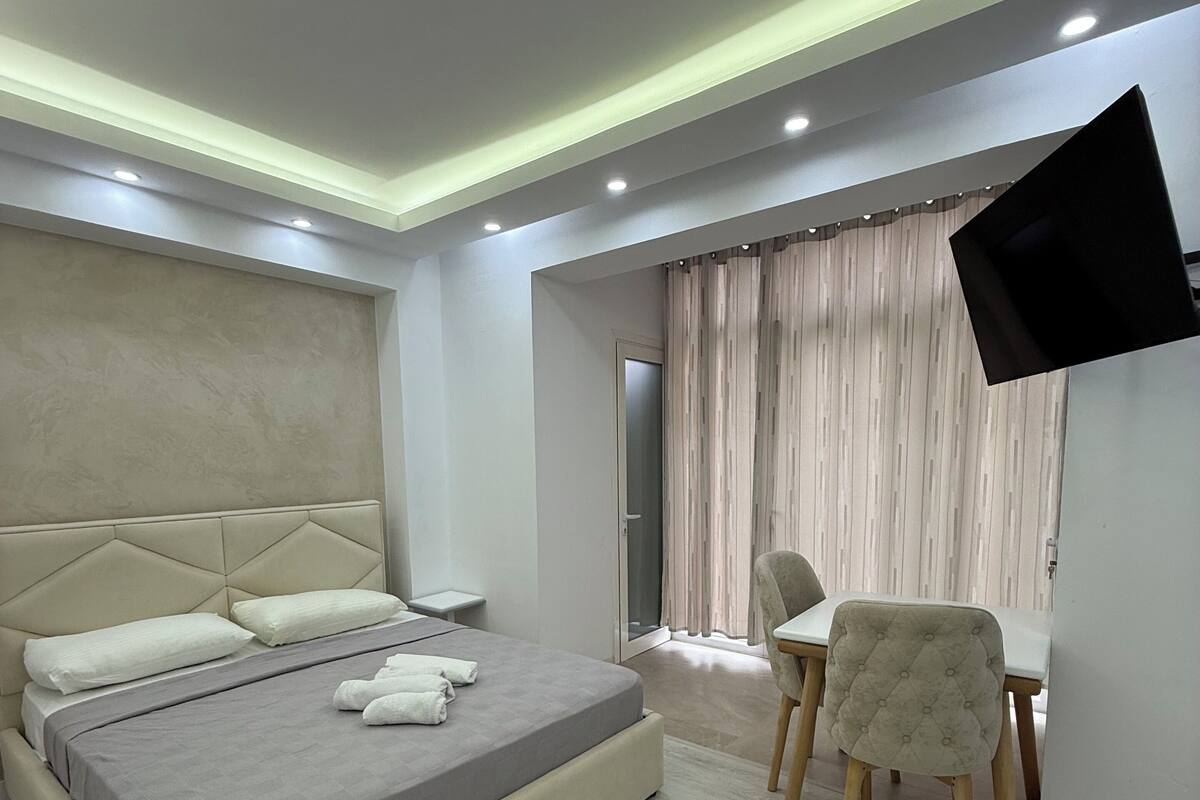 A modern bedroom with a bed, bedside table, chair, and a TV mounted on the wall.