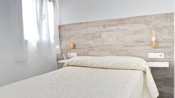 Une chambre moderne avec un grand lit, une table de chevet, une lampe fixée au mur et une prise de courant.