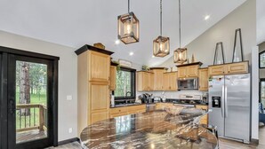 Une cuisine moderne avec des meubles en bois, un grand îlot central, des appareils en acier inoxydable et des luminaires suspendus.