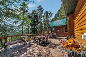 Une cabane en bois dotée d’un patio comprenant une table et des chaises, entourée d’une terrasse en bois et d’une rambarde.