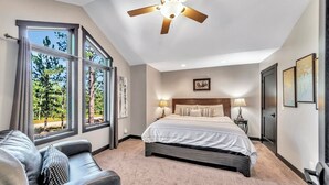 Une chambre avec un grand lit, un ventilateur de plafond, une fenêtre donnant sur les arbres et une table de chevet avec des lampes.
