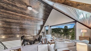Ein modernes Interieur mit einem großen Fenster, einem Sofa, einem Sessel und einer dekorativen Tiermaske.