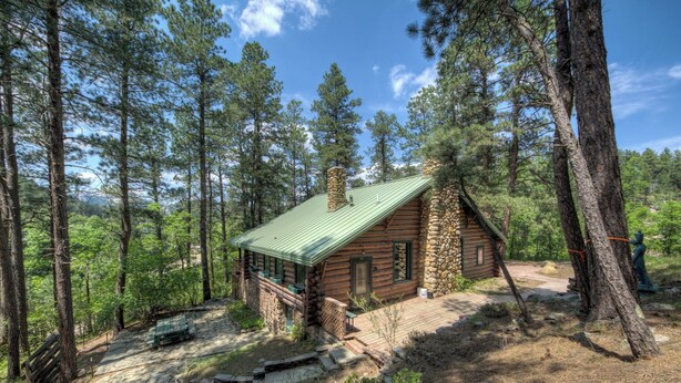 A log cabin with a stone chimney, surrounded by tall pine trees. - 1927 Cabin of Keystone (Keystone)