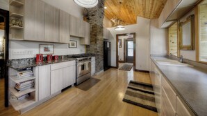 A modern kitchen with granite countertops, white cabinets, a stone column, and a wooden ceiling. - 1927 Cabin of Keystone (Keystone)