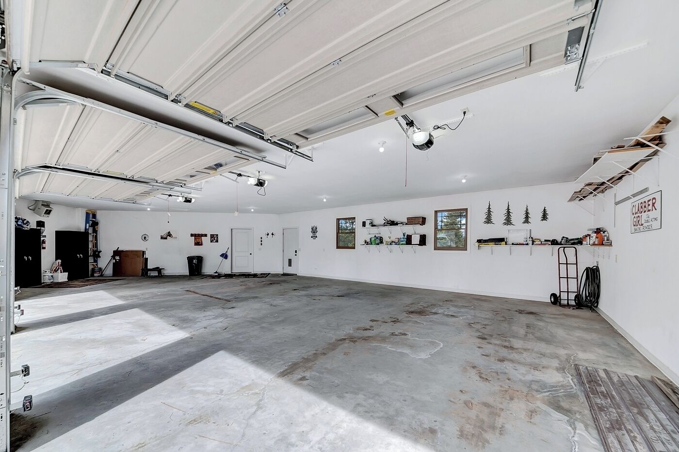 A spacious garage with a concrete floor, white walls, and a high ceiling with exposed beams and lighting fixtures.
