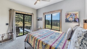 A bedroom with a large bed, a ceiling fan, a view of the outdoors, and a painting on the wall. - Hillside Lodge of the Black Hills (Sturgis)