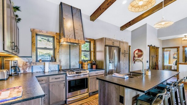 A modern kitchen with a central island, stainless steel appliances, and wooden beams. - Hillside Lodge of the Black Hills (Sturgis)