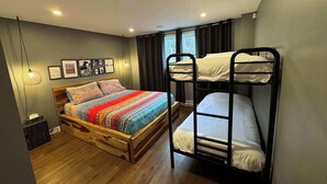 A room with a wooden bed, a bunk bed, a small wooden chest, and a wall-mounted light fixture.
