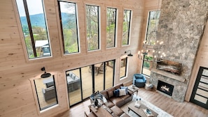 Amplia sala de estar con chimenea de piedra, ventanas grandes y una terraza de madera.