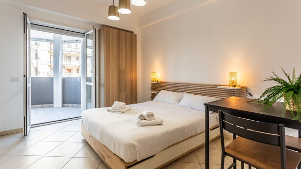 A modern hotel room with a bed, a dining table, and a view through a sliding door to an outdoor balcony. - Cloud Swing Room 1 by Wonderful Italy (Bari)