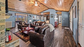 A spacious living room with a wooden ceiling, leather sofas, a coffee table, and a fireplace. - Stunning 3BD Cabin w/ VIEWS! Game Room + HOT TUB! (Gatlinburg)