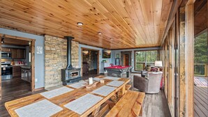 A spacious living area with a wooden ceiling, stone walls, a fireplace, a pool table, and a large window overlooking greenery. - Stunning 3BD Cabin w/ VIEWS! Game Room + HOT TUB! (Gatlinburg)