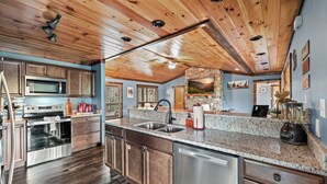 A modern kitchen with wooden ceiling beams, stainless steel appliances, granite countertops, and a stone backsplash. - Stunning 3BD Cabin w/ VIEWS! Game Room + HOT TUB! (Gatlinburg)