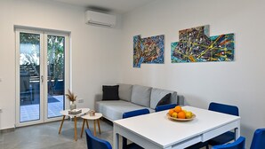 A modern living room with a grey sofa, a white dining table with blue chairs, and abstract paintings on the wall.