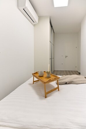 A minimalist bedroom with a bed, a small wooden table with a cup and candle, and an air conditioning unit mounted on the wall. - Apartment Judy, Terrace&Garden, 80m from the Beach (Sv. Filip I Jakov)