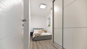 A modern bedroom with a bed, bedside table, and a small plant on a shelf.