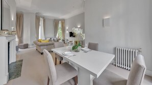 A modern living room with a white sofa, a dining table set for two, and a fireplace. - Cosy One Bedroom Behind Harrods (Greater London)