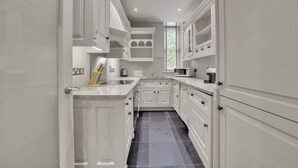 A narrow kitchen with white cabinetry, a countertop, and a window. - Cosy One Bedroom Behind Harrods (Greater London)