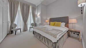 A bedroom with a large bed, two bedside lamps, a chair, and a desk. - Cosy One Bedroom Behind Harrods (Greater London)