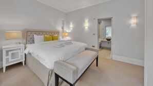 Een moderne hotelkamer met een groot bed, nachtkastjes, een bankje en een badkamer zichtbaar door een geopende deur.