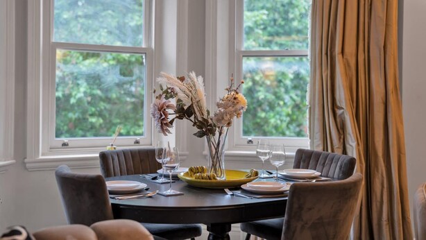 Een eettafel gedekt voor twee personen, met een bloemetjesvaas, borden en glazen.