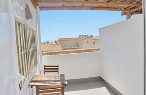 Ein kleiner Balkon mit Holztisch und -stühlen, einem Metallgitter und Blick auf Gebäude und das Meer.