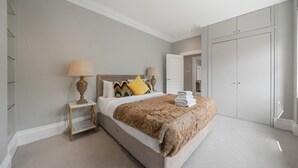 Ein Schlafzimmer mit einem großen Bett, zwei Nachttischen, einem Kleiderschrank und einer Tür zu einem anderen Raum.
