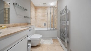 Ein modernes Badezimmer mit Duschkabine aus Glas, Badewanne, Toilette und Waschtisch mit Spiegel.