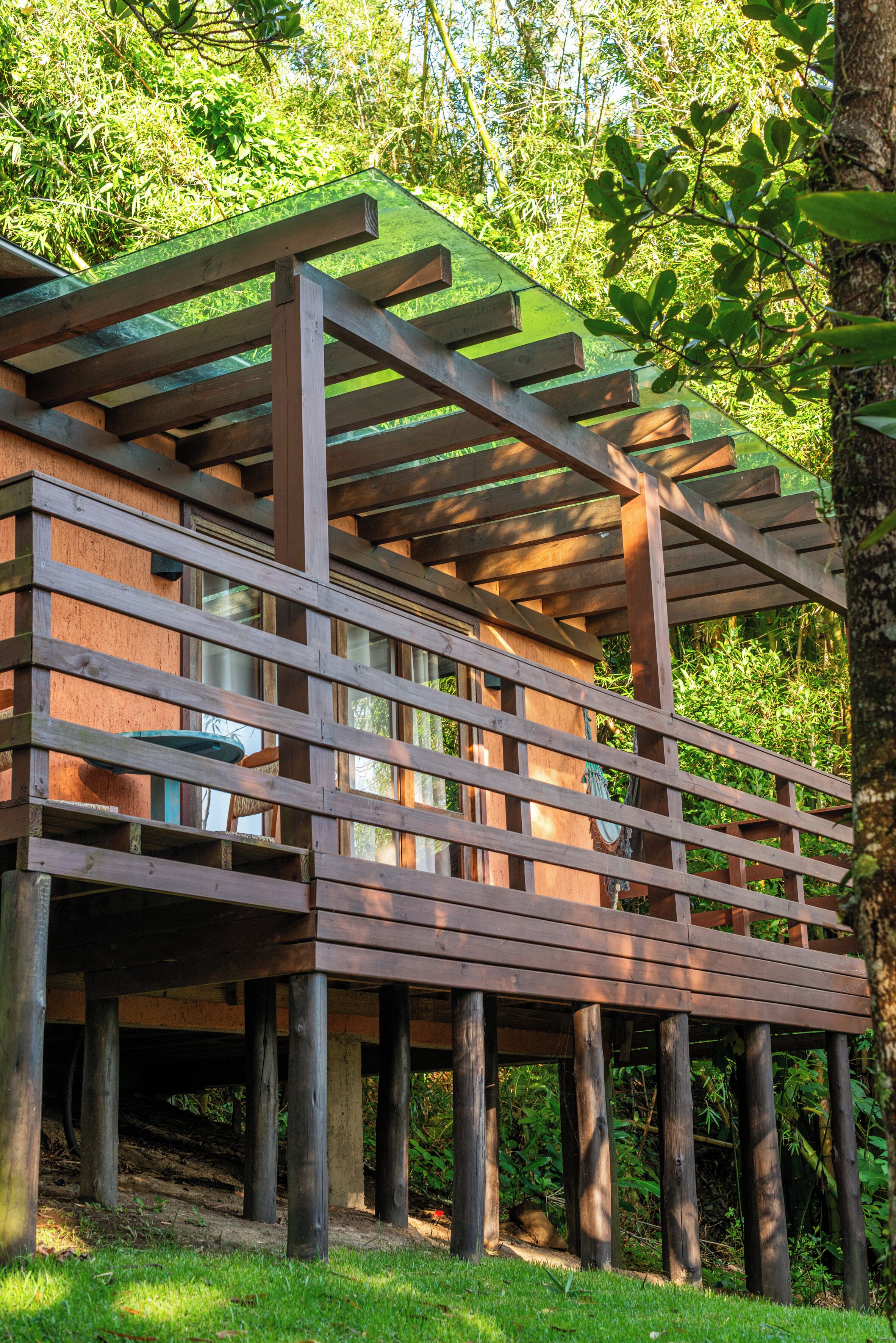 A wooden deck with a pergola structure, surrounded by lush greenery.