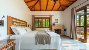Una camera da letto con un letto grande, travi in legno a soffitto, un camino e vista sul verde dalla finestra.
