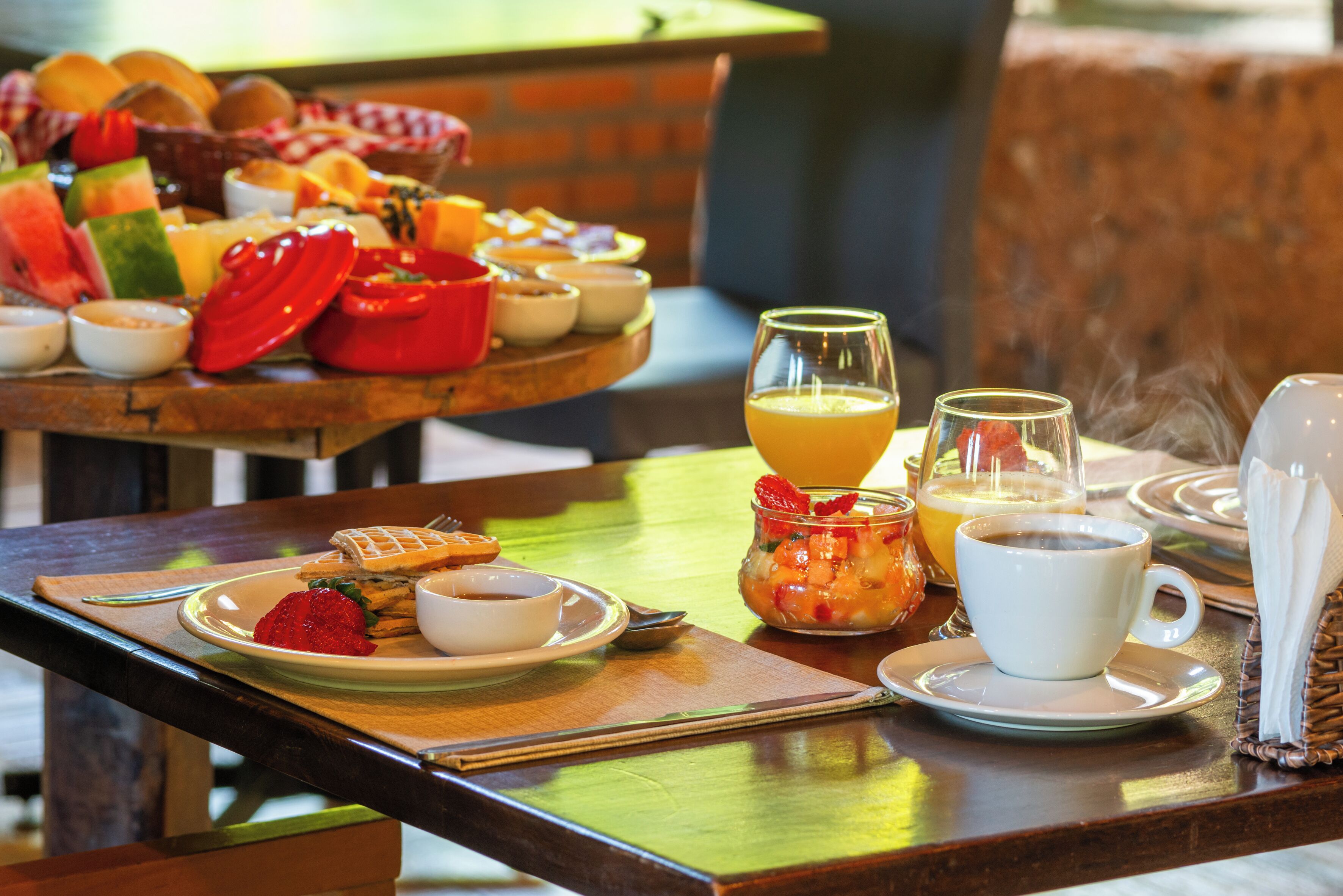 Una mesa de desayuno con diversos alimentos, un vaso de zumo de naranja y una taza de café.