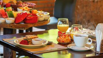 Una mesa de desayuno con diversos alimentos, un vaso de zumo de naranja y una taza de café.