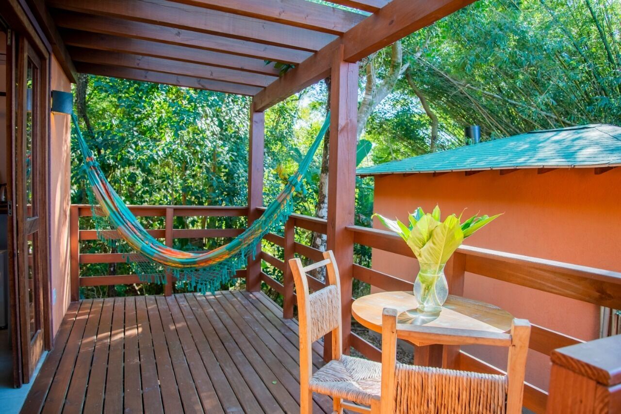 Una terraza de madera con una hamaca, sillas de mimbre y una mesa con un florero.