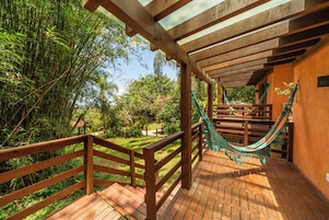 Una terraza de madera con una hamaca y vistas a un jardín exuberante.