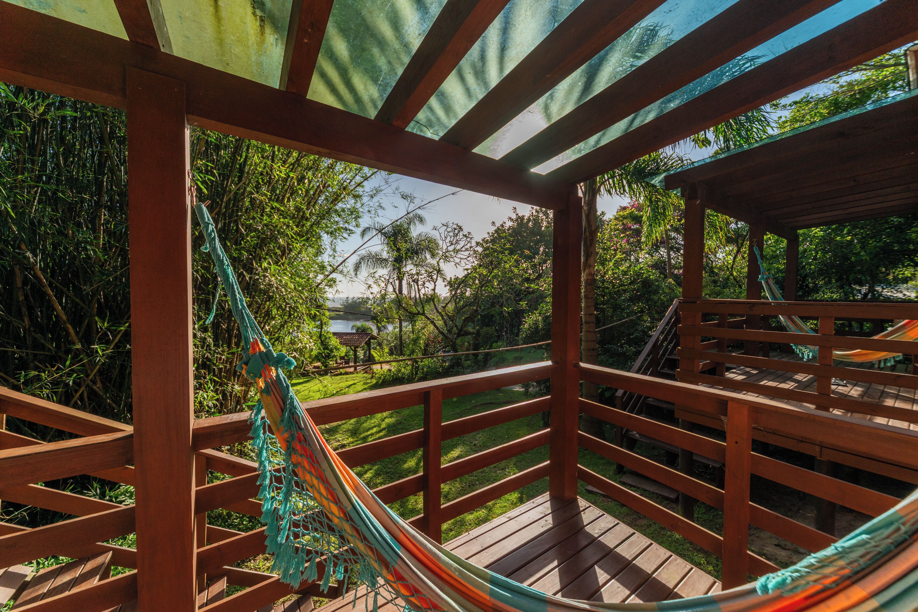 Una terraza de madera con una hamaca y vistas a un jardín exuberante y edificios lejanos.