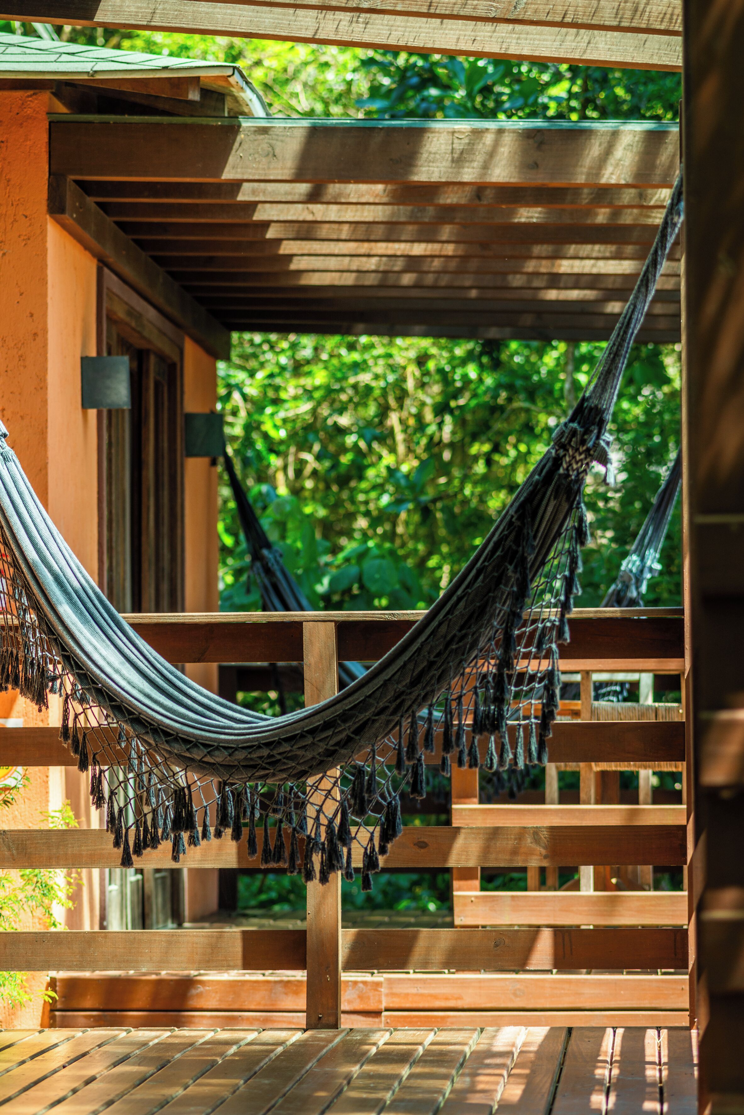 A hammock hanging between wooden beams in a covered outdoor area with a view of lush greenery.