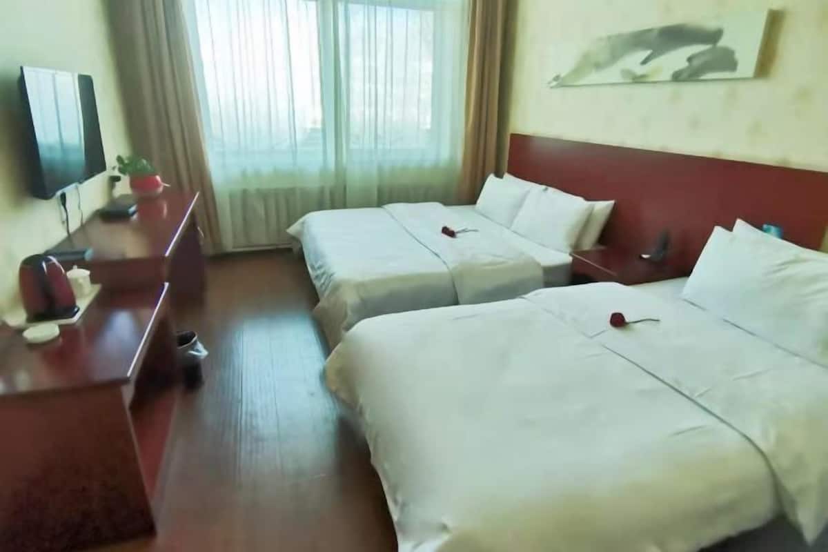A hotel room with two beds, a desk, a TV, and a window with curtains.