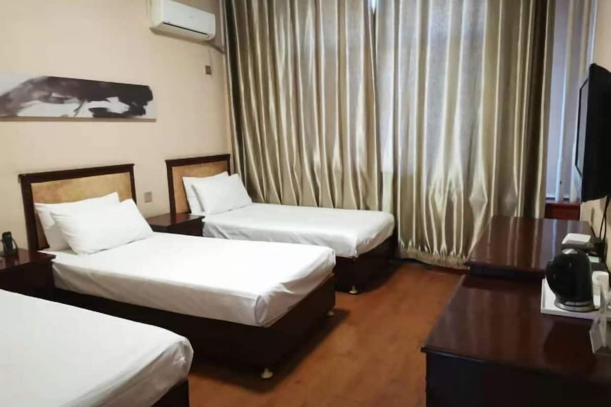 A hotel room with two single beds, a wooden desk, a black coffee maker, and a large window with curtains.