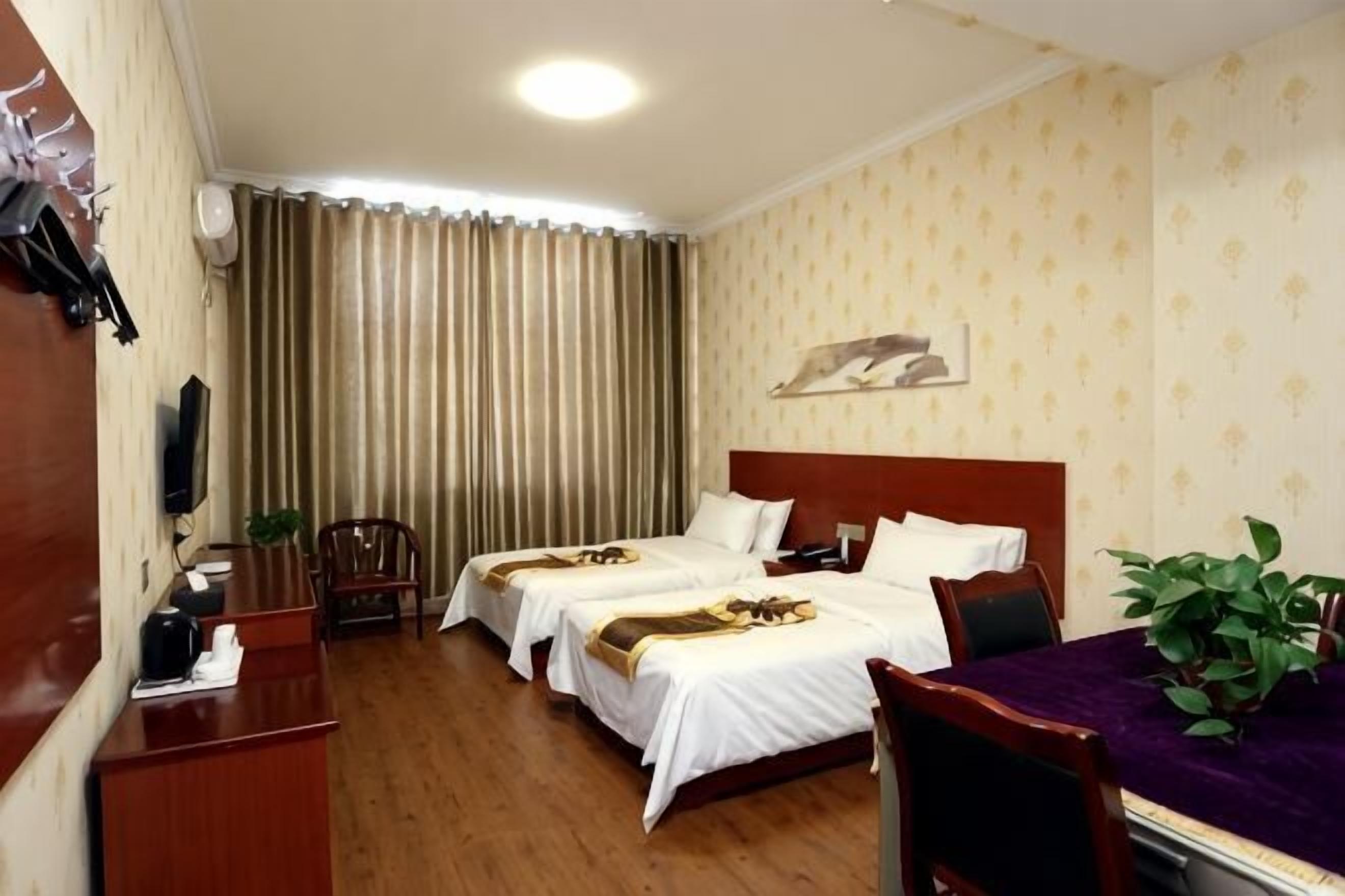 A hotel room with two beds, a desk, a chair, a TV, and a window with curtains.