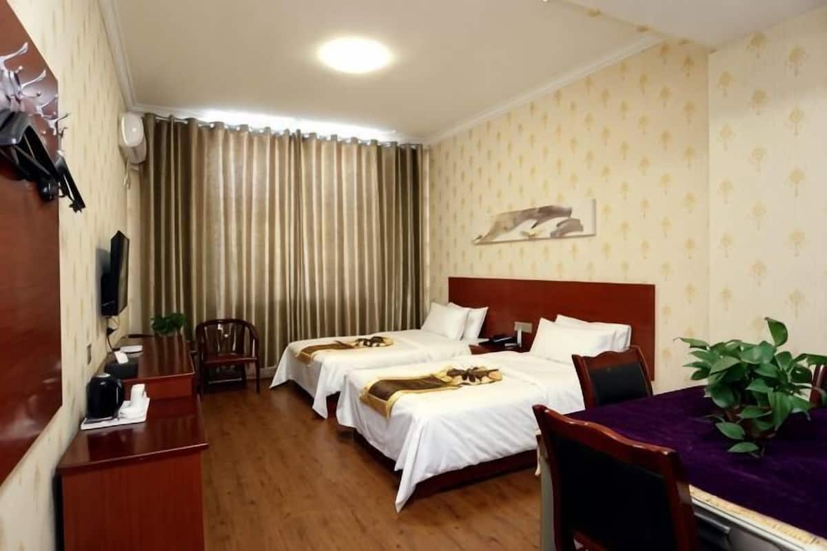 A hotel room with two beds, a desk, a chair, a TV, and a window with curtains.