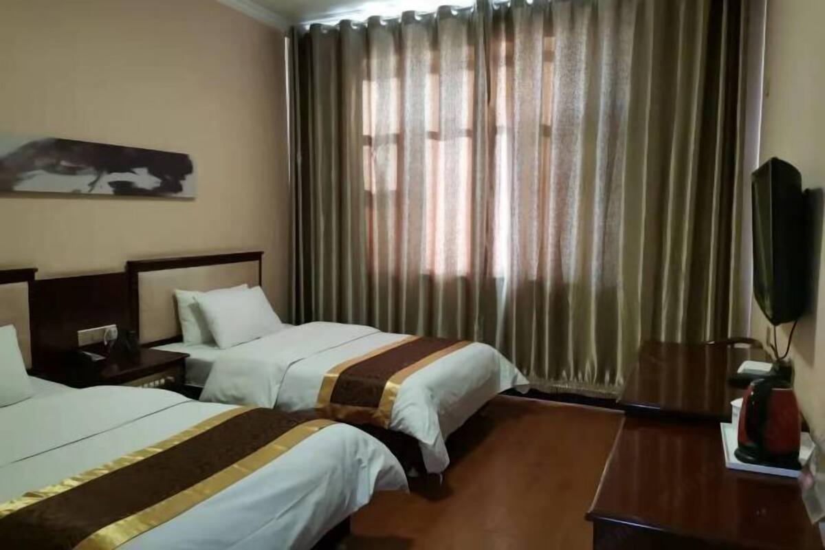 A hotel room with two beds, a flat-screen TV, a wooden nightstand, and a large window with curtains.