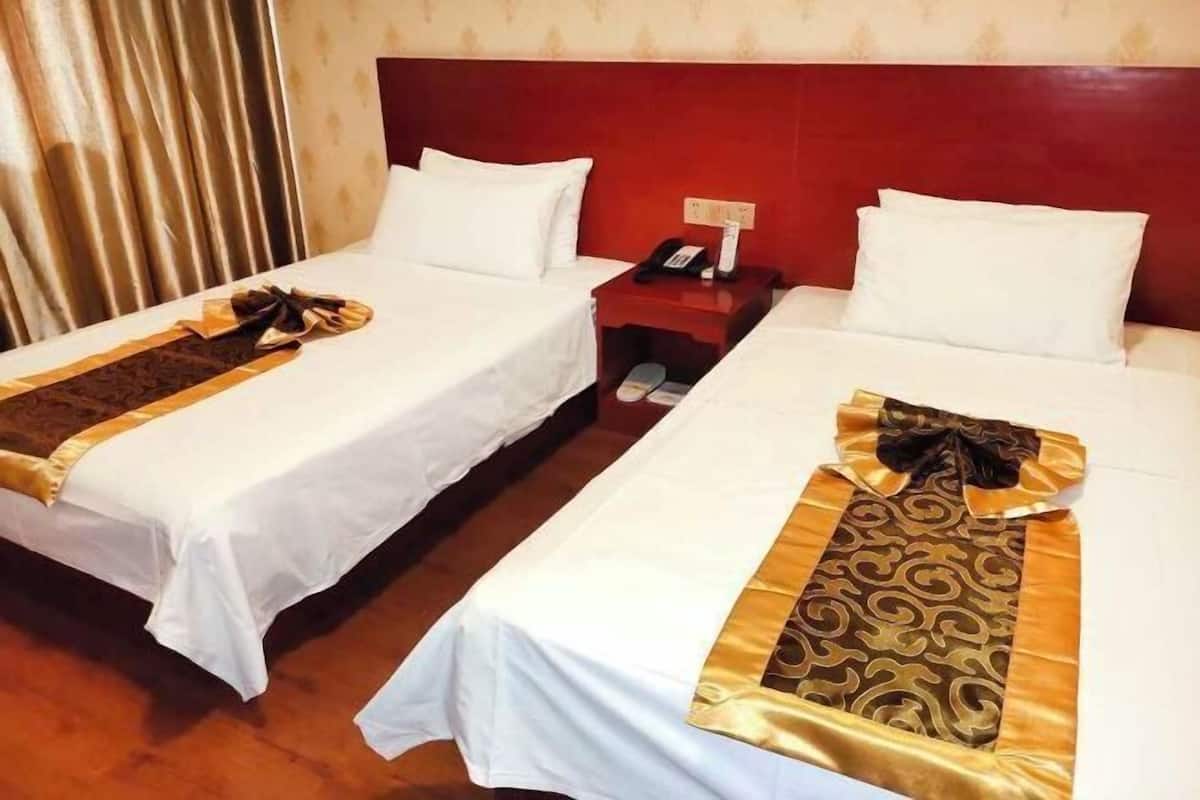 Two single beds with white linens and decorative headboards, a wooden floor, and a nightstand with a phone and lamp.