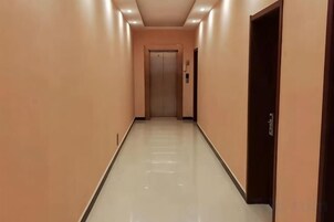 Un pasillo con una puerta al final, un interruptor de luz y un dispositivo fijado a la pared.